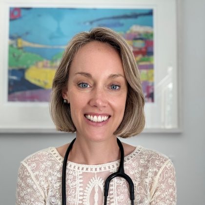 Dr Jessica Dawkins smiles at the camera. she has short blonde hair and is wearing a stethoscope around her neck.