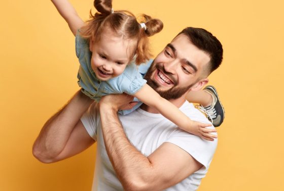 Father lifting up daughter in a playful way on a yellow background